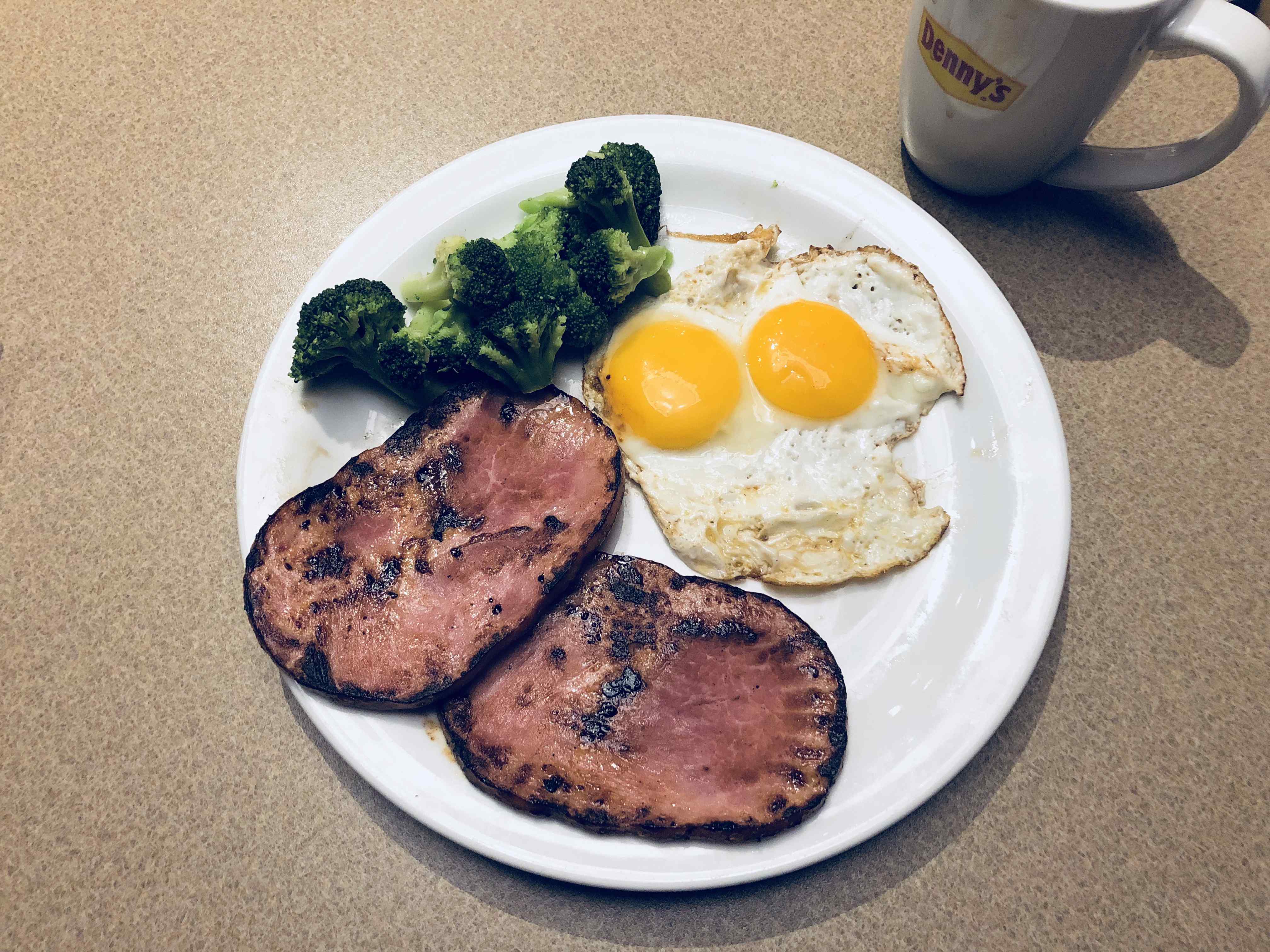Denny&rsquo;s breakfast with two fried eggs, two slices of grilled ham, and broccoli